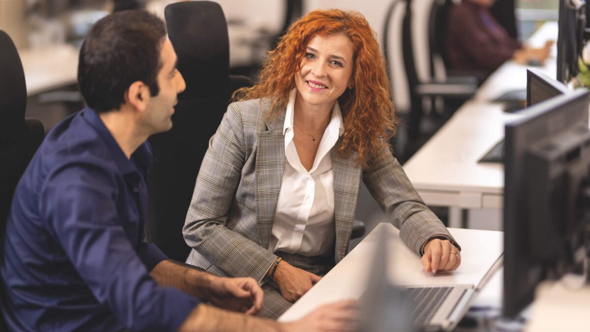 a woman and a man in an office sitting at a desk with a computer on it